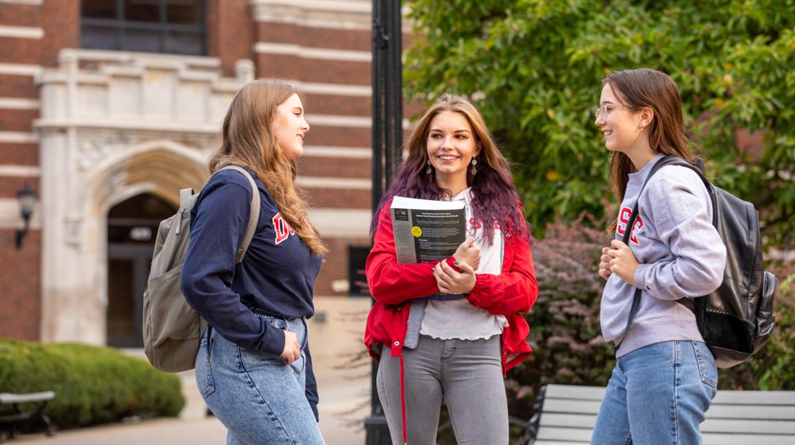 Image of three students conversing on campus with Canevin Hall in background