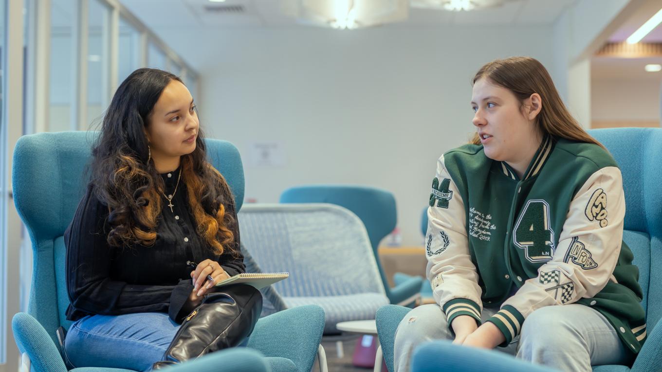Psy.D. School Psychology graduate engaging in session with high school student sitting in chairs next to each other in school building.