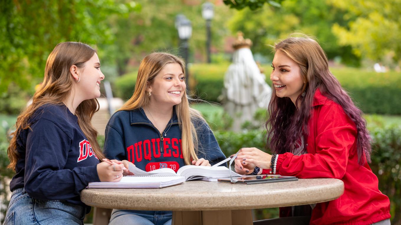 Three students studying around table outside