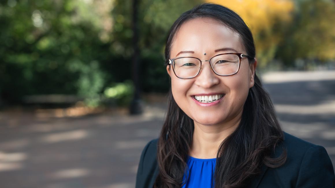 Dr. Xia Chao headshot against outdoor campus background with trees