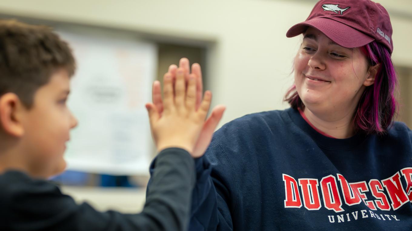 Young client connecting and smiling and engaging while high fiving M.S.Ed. Applied Behavior Analysis graduate in client ABA session.