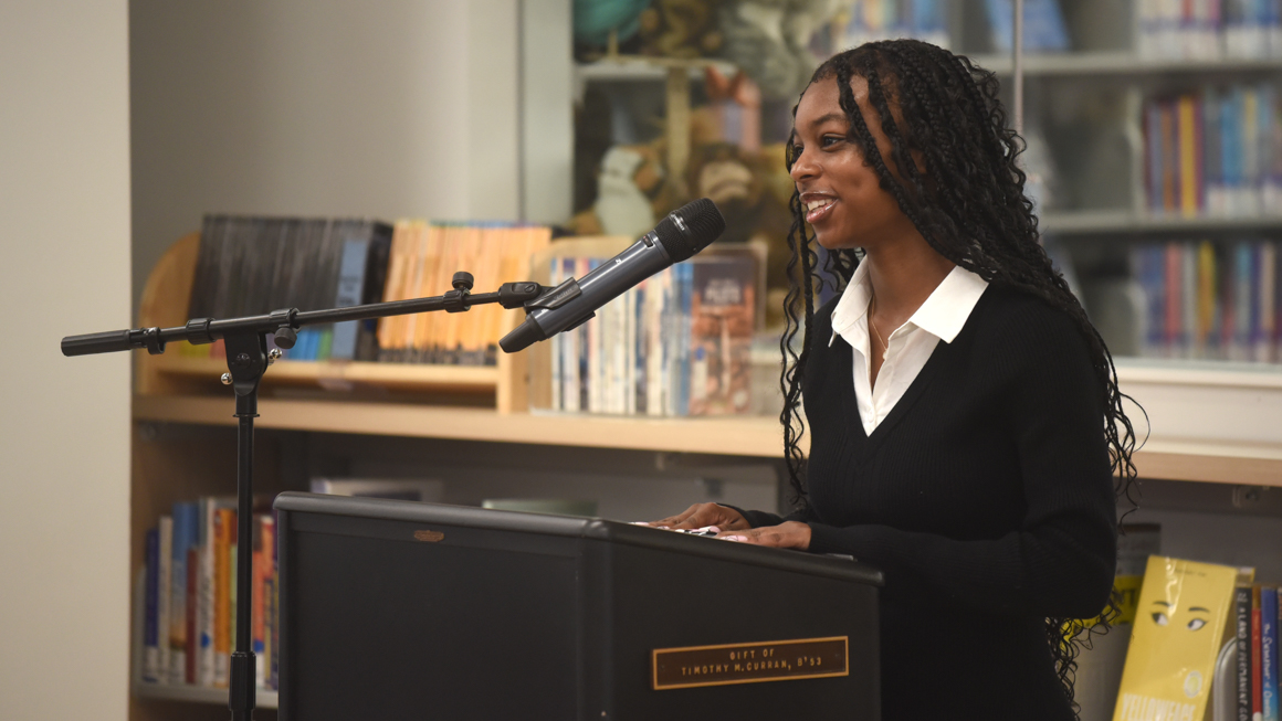 School of Education's Jayla Flenory giving speech at podium smiling in the library.