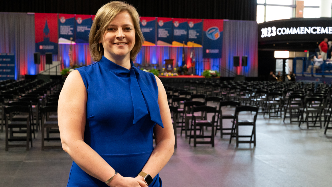 Alum Kara Eckert smiling on School of Education Commencement floor with the stage behind her