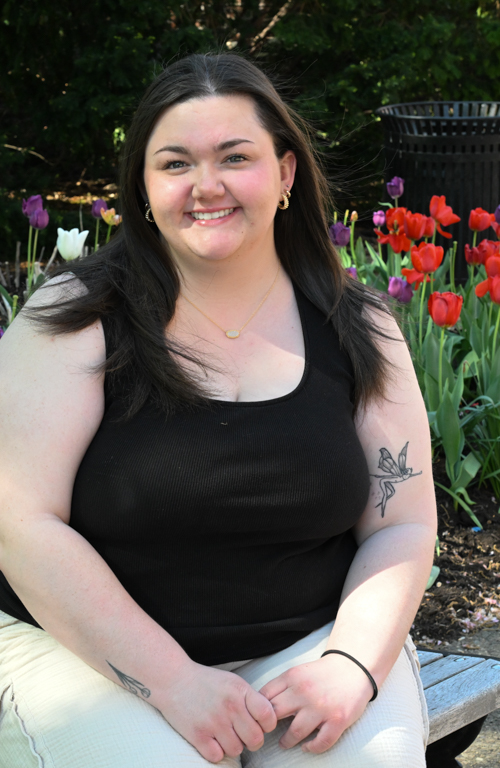 School of Education student Cassidy Klock smiling sitting on bench outside on camps with tulips in the background.
