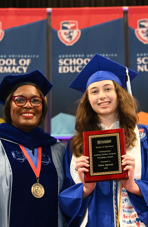 Jillian Spernak with undergraduate award in hand smiling on stage next to School of Education Dean Generett.