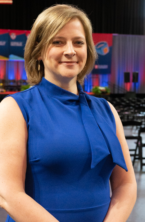 Alum Dr. Kara Eckert smiling on School of Education Commencement floor with the stage behind her