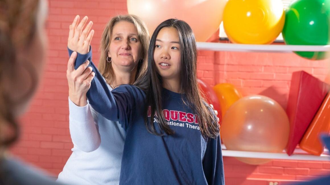 Dr. Retta Martin demonstrates a mobility exercise with the help of an OT student.