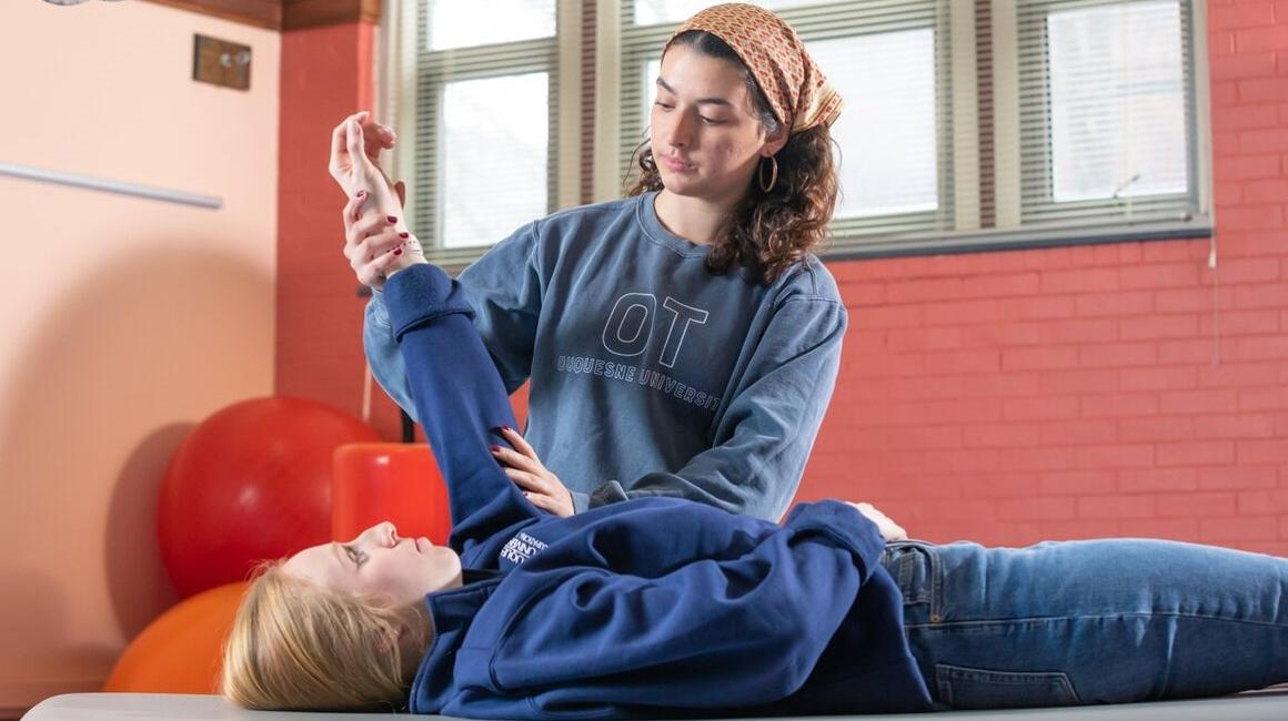 One OT student demonstrates a mobility exercise on another OT student.