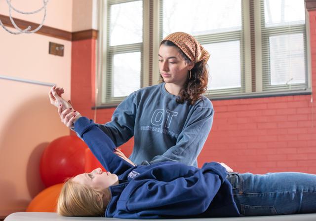 Two OT students learning how to position a student in a hospital bed.