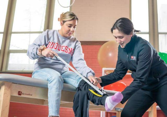A faculty member helping an OT student measure their leg for splinting.