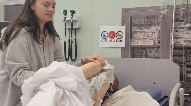 Student in lab learning how to roll a patient dummy in bed.