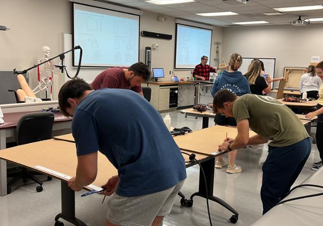 Three students in the Assistive Technology lab cutting cardboard for a project.