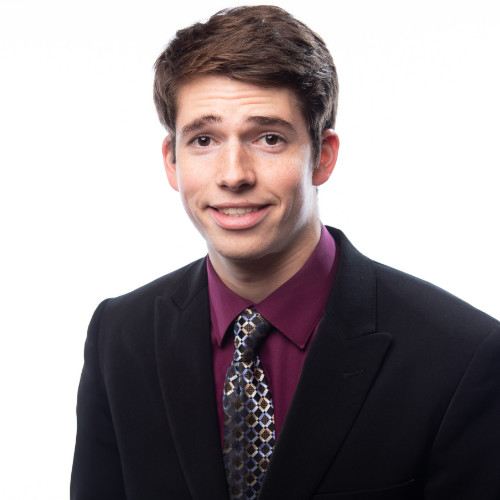 Headshot photo of Bryan Whitaker smiling in black suit with tie