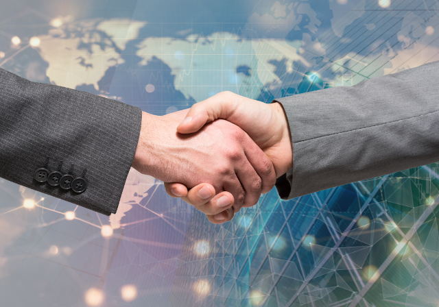 A closeup of two hands shaking in front of a background of a building and a map of the world. 