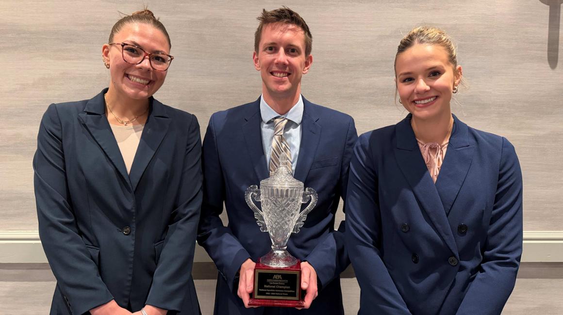 Three people standing and smiling holding trophy