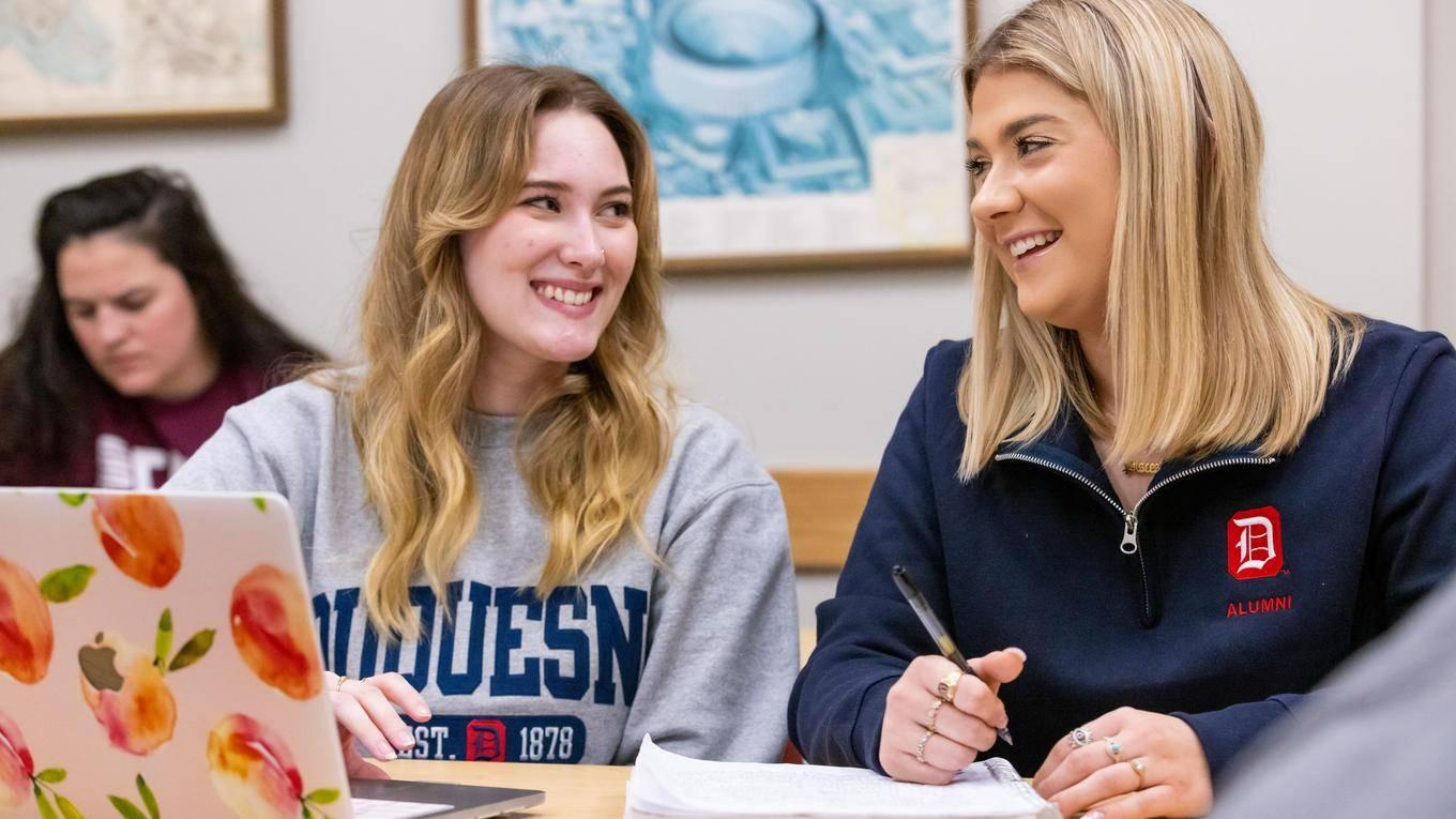 Two female students working on a group project on a laptop