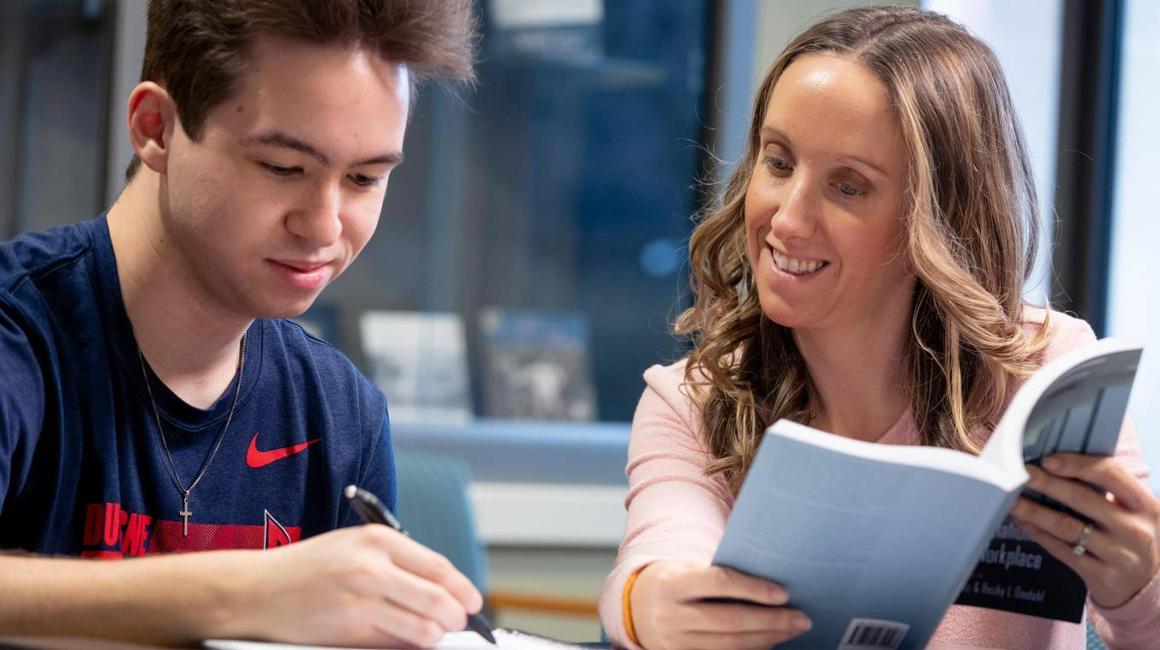 One male student and one female student taking notes on a book they are reading