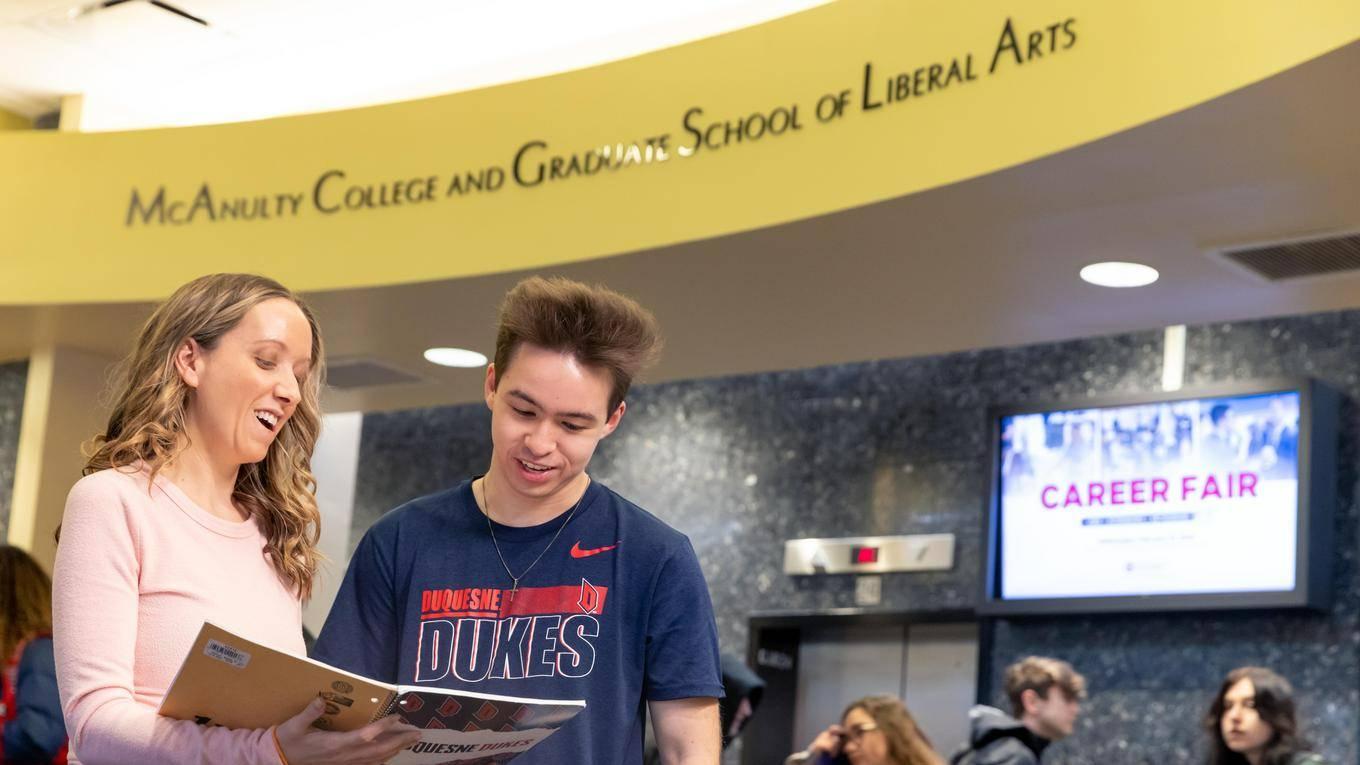Two students sharing notes in a notebook in the College Hall lobby