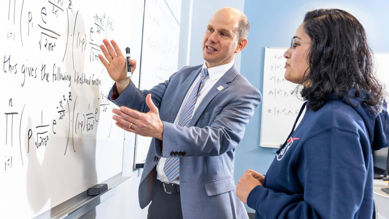 Math professor working on a problem on a white board with a student