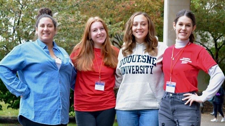 Two female student ambassadors smiling for the camera with two of our College Office staff.