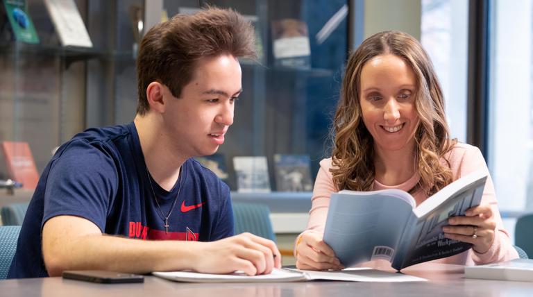 Male and female student reading a book in the College Hall lobby