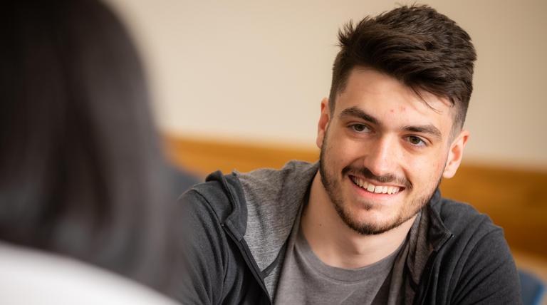 White male student smiling towards camera while talking to a University employee.