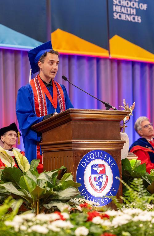 Student speaker addressing the crowd from the podium at Duquesne University commencement.