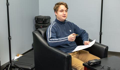 Male student conducts an interview with recording equipment in front of him.