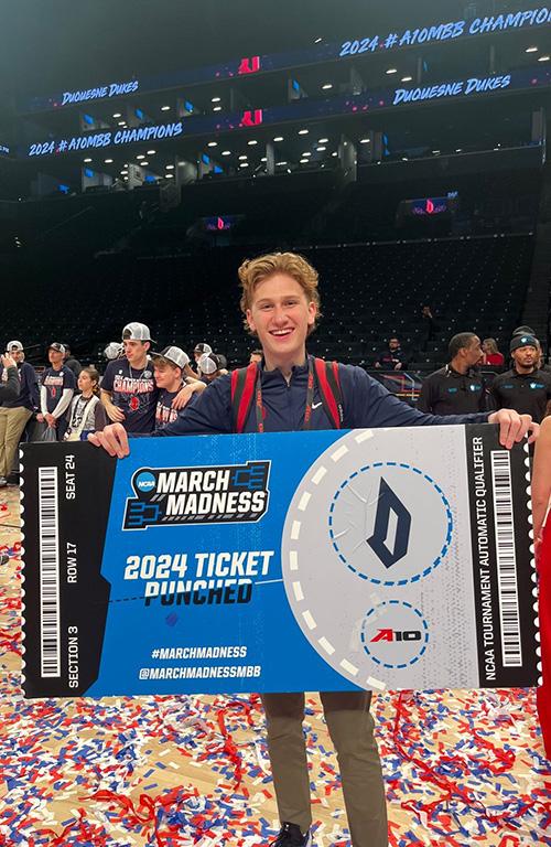 Jack Morgan holding an oversized A10 2024 ticket with confetti falling down on a basketball court.