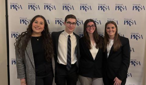 Four Duquesne students in front of a Pittsburgh PRSA step-and-repeat during the organization's annual award ceremony.