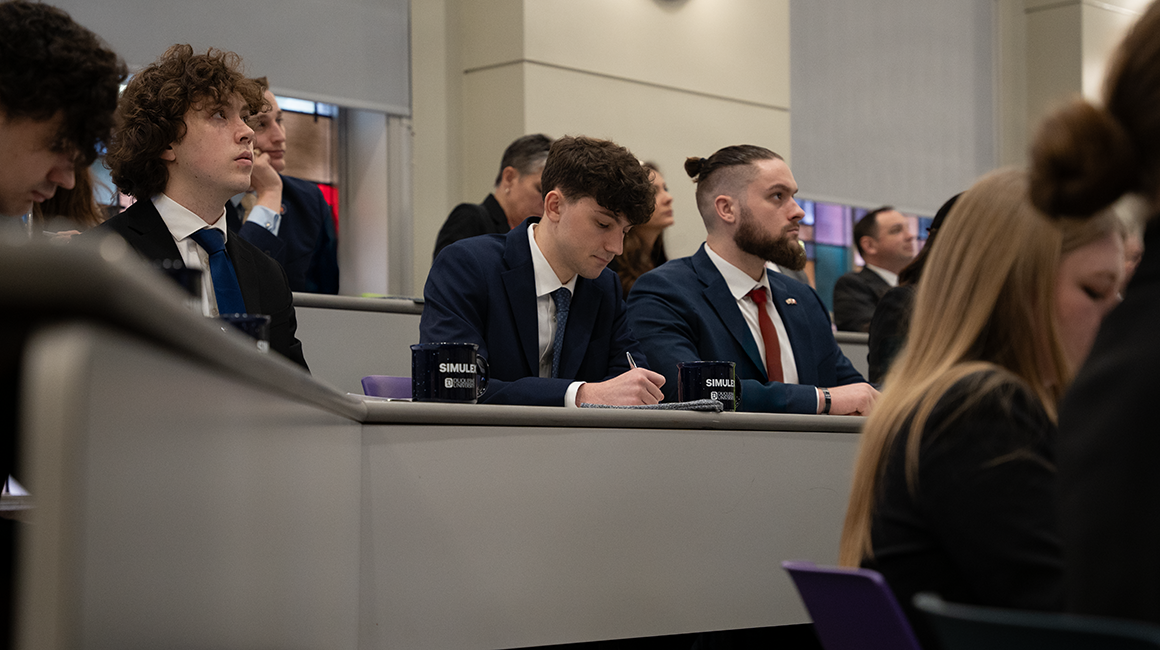 Three male students in a lecture hall taking notes.