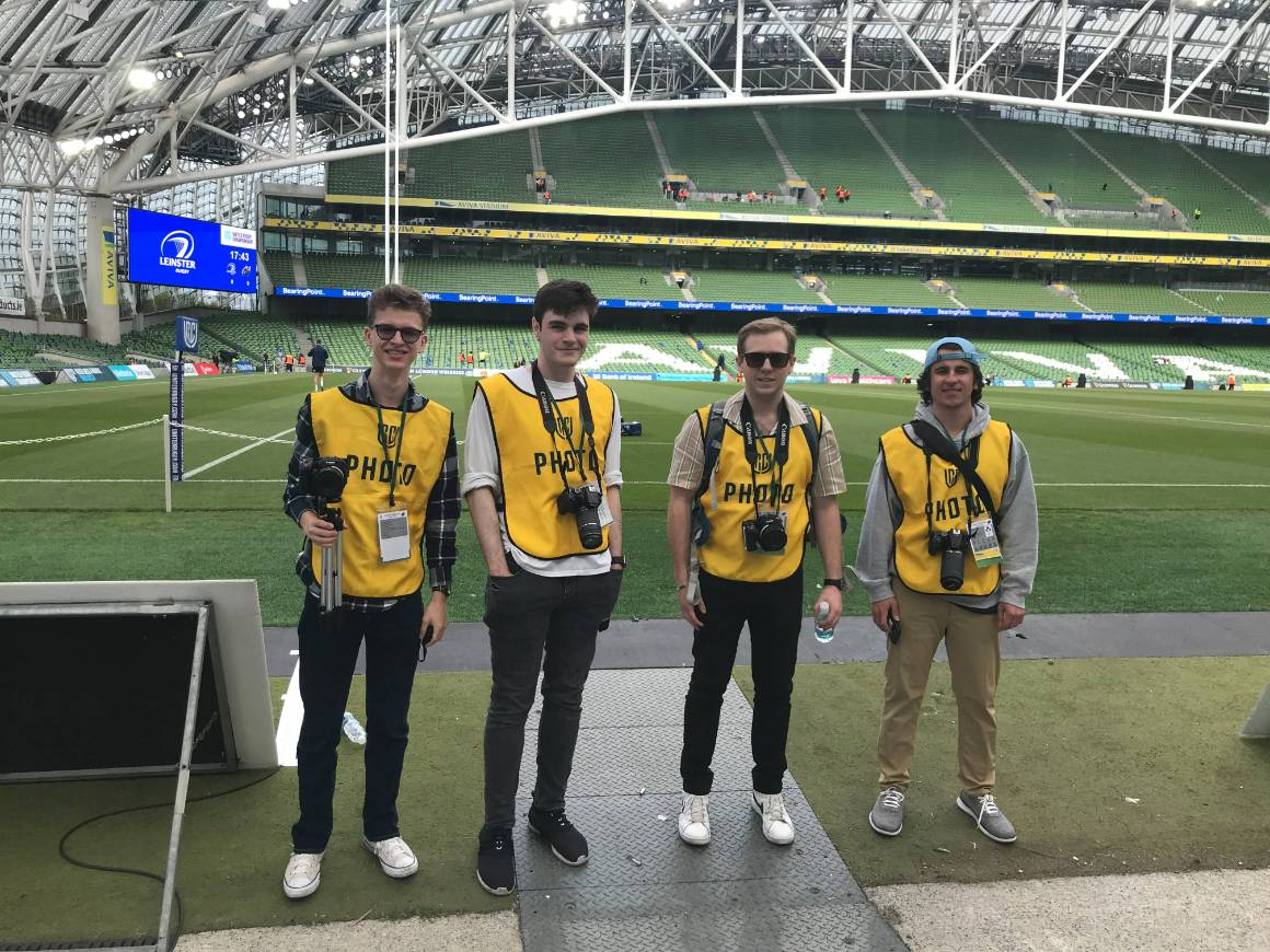 4 students posing for the camera on the sidelines of a rugby field