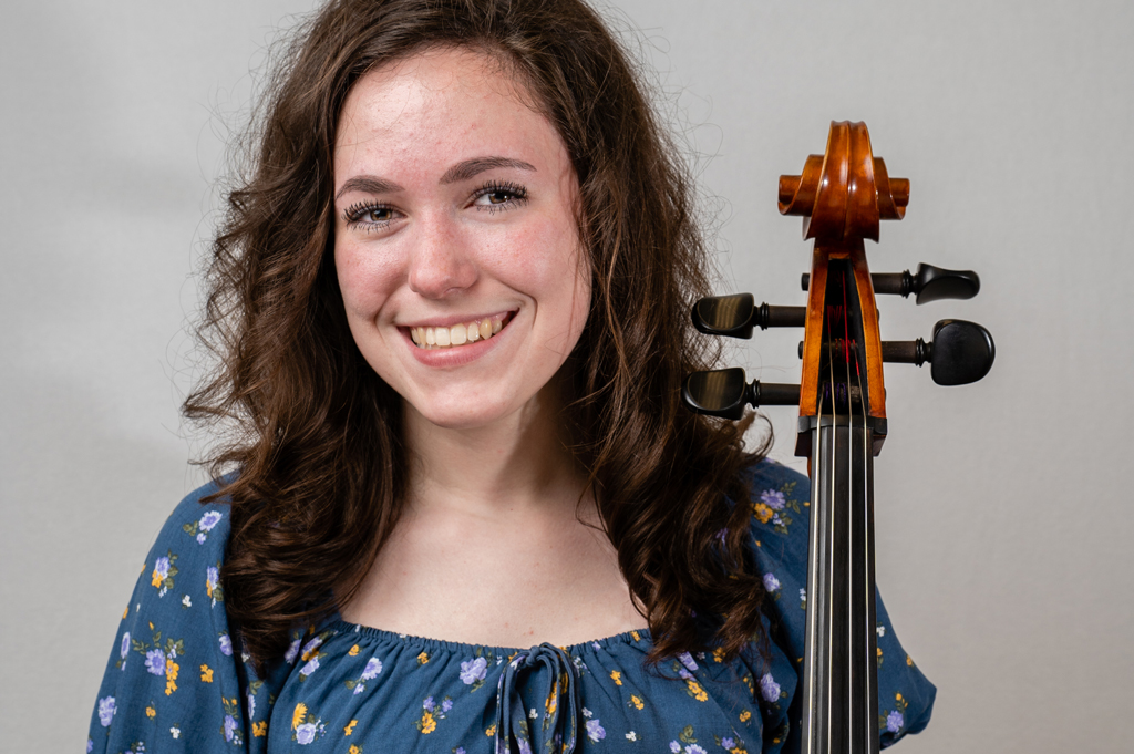 A cellist holds a cello in this headshot.