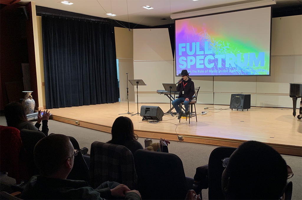 A person performs on stage in front of a projected backdrop that reads Full Spectrum.
