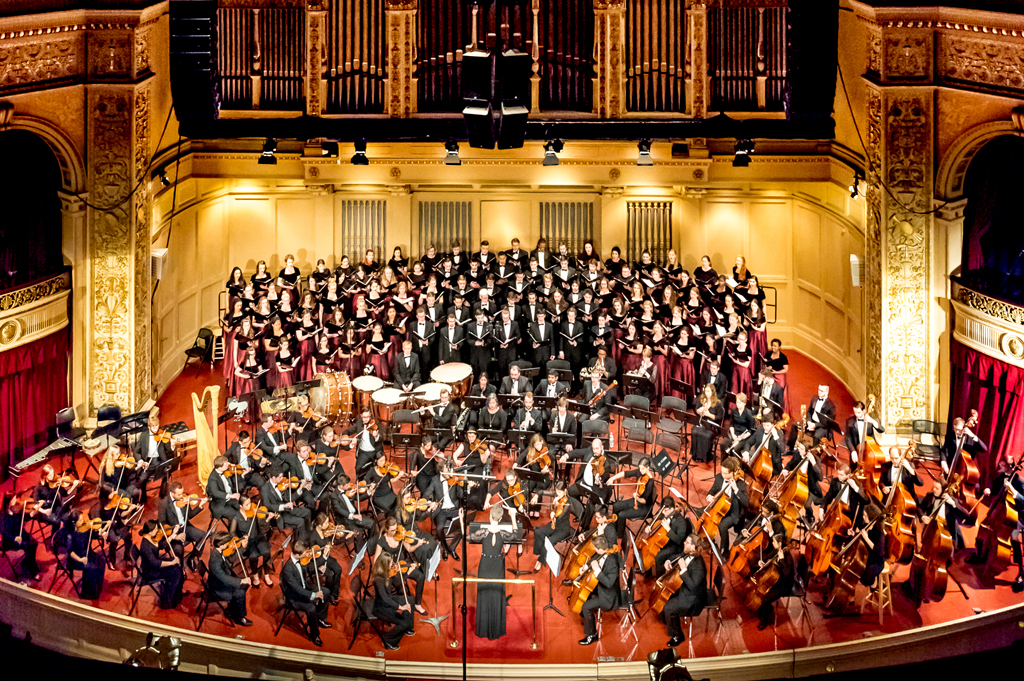 Orchestra and choirs perform on stage.