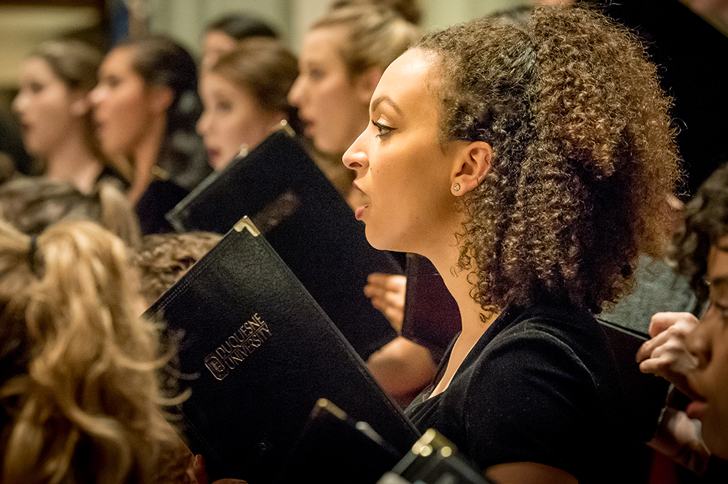 A woman holding a Duquesne University choir folder sings in concert.