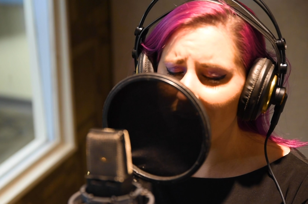 A singer wearing headphones records vocals in an isolation booth.