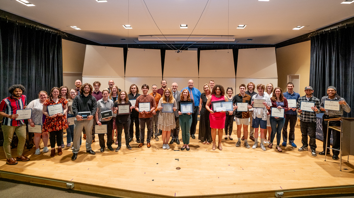 Award winners pose with presenters on a stage.