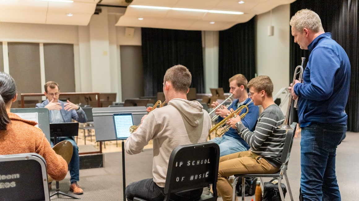 Trumpet teacher looks on while trumpet students rehearse..