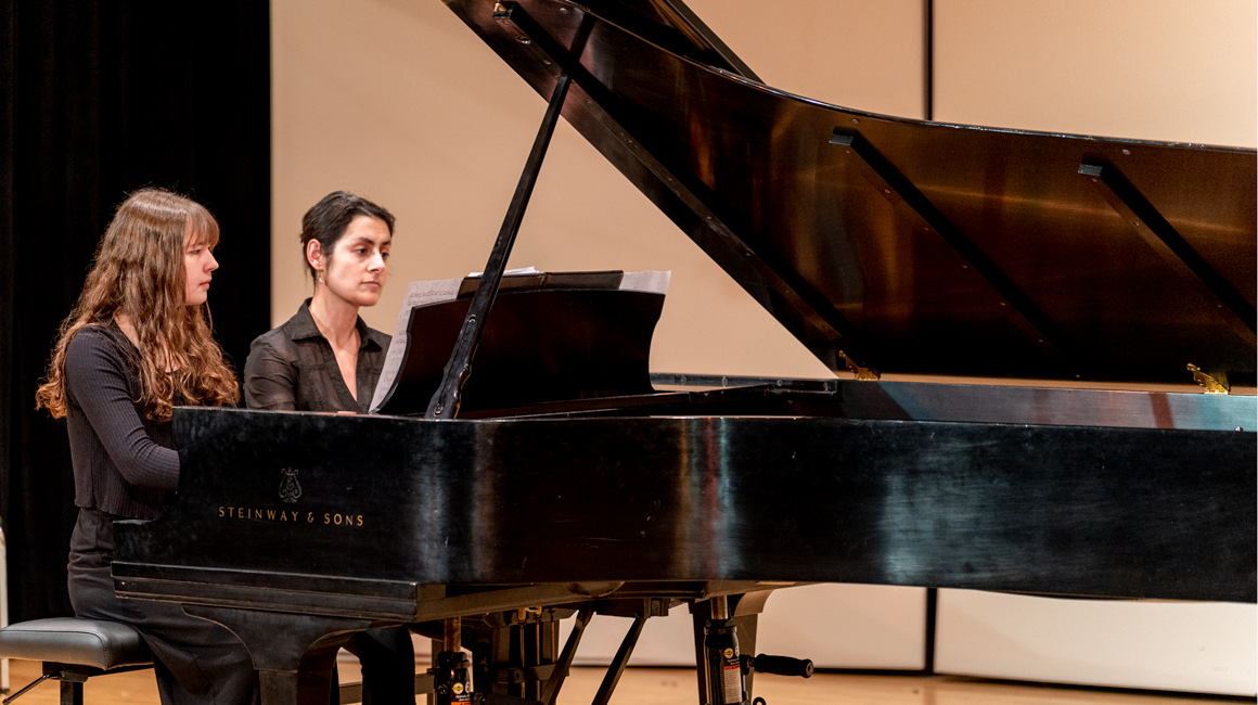 A student and professor perform on a piano.