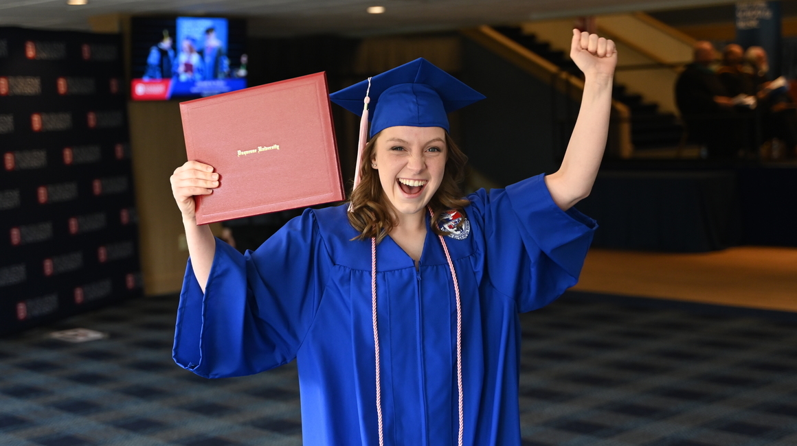 A graduting student celebrates with diploma cover in hand.