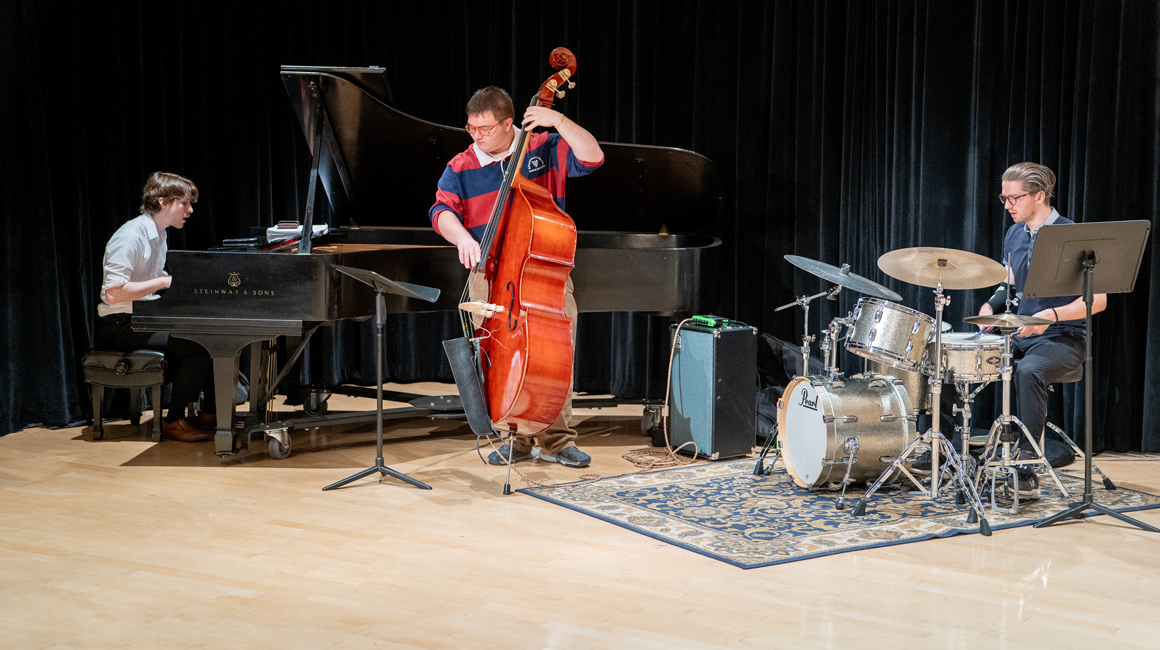 A trio of jazz students perform on piano, bass, and drums.