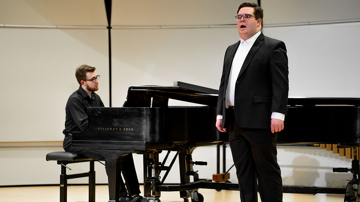 A singer performs in a tuxedo with a piano player accompanying him.