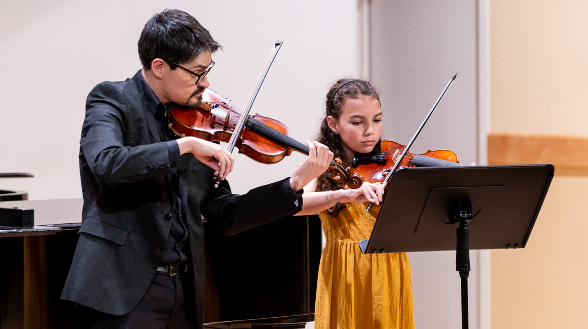 Student and teacher perform together on violins.