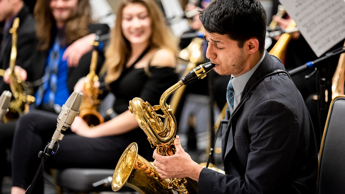 A male student plays a baritone saxophone in a concert setting.