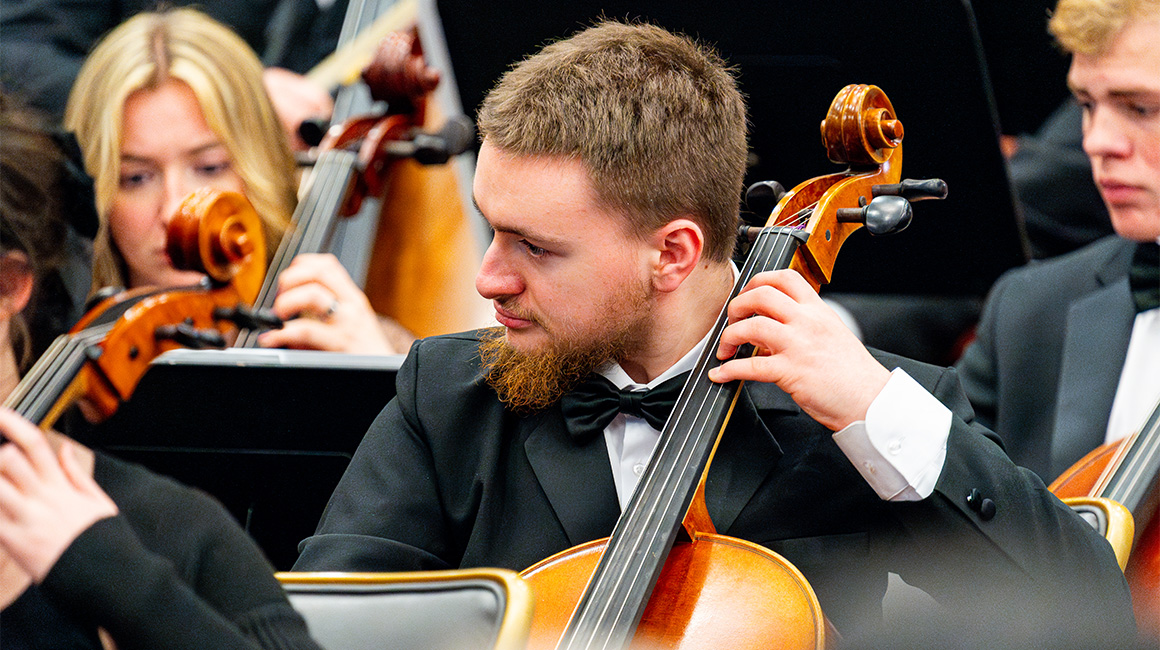 Closeup photo of a cellist wearing a tuxedo while performing in a group.