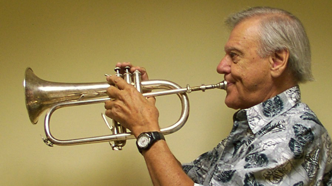 A man in a Hawaiian shirt plays a flugelhorn.