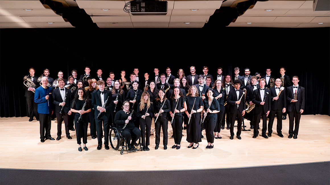 Wind Symphony poses for a group photo in front of a black curtain.