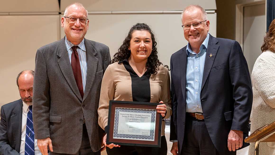 Student poses with their award, alongside Dean and Department Chair for a photo.