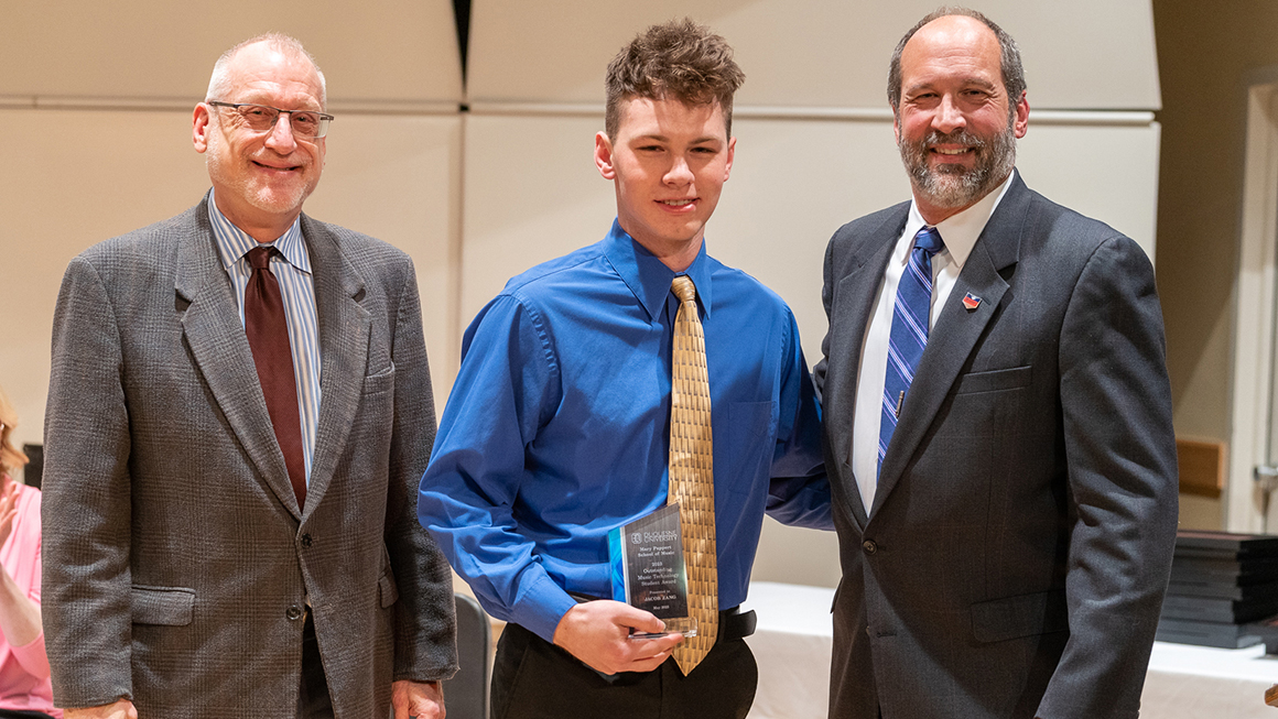 Student poses with their award, alongside Dean and Department Chair for a photo.